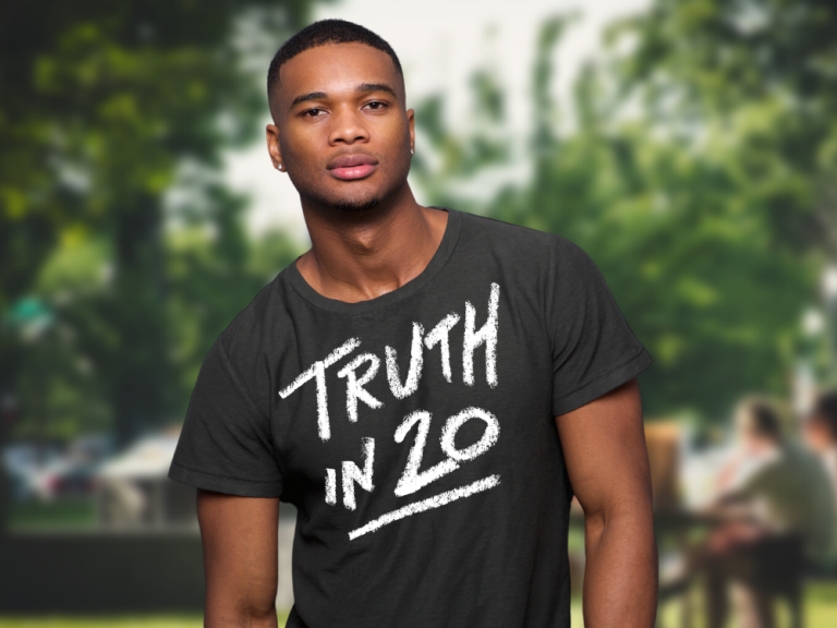 Young man wearing Truth in 20 tshirt standing with blurred park in background