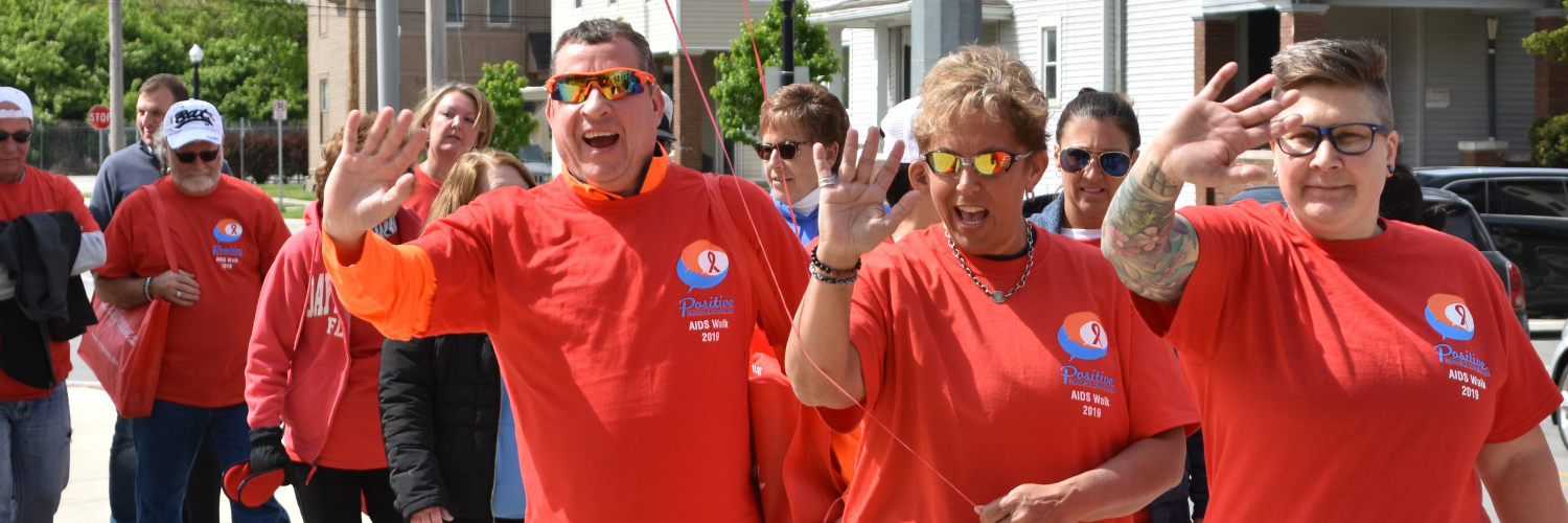Smiling waving people wearing matching red shirts at AIDS Walk