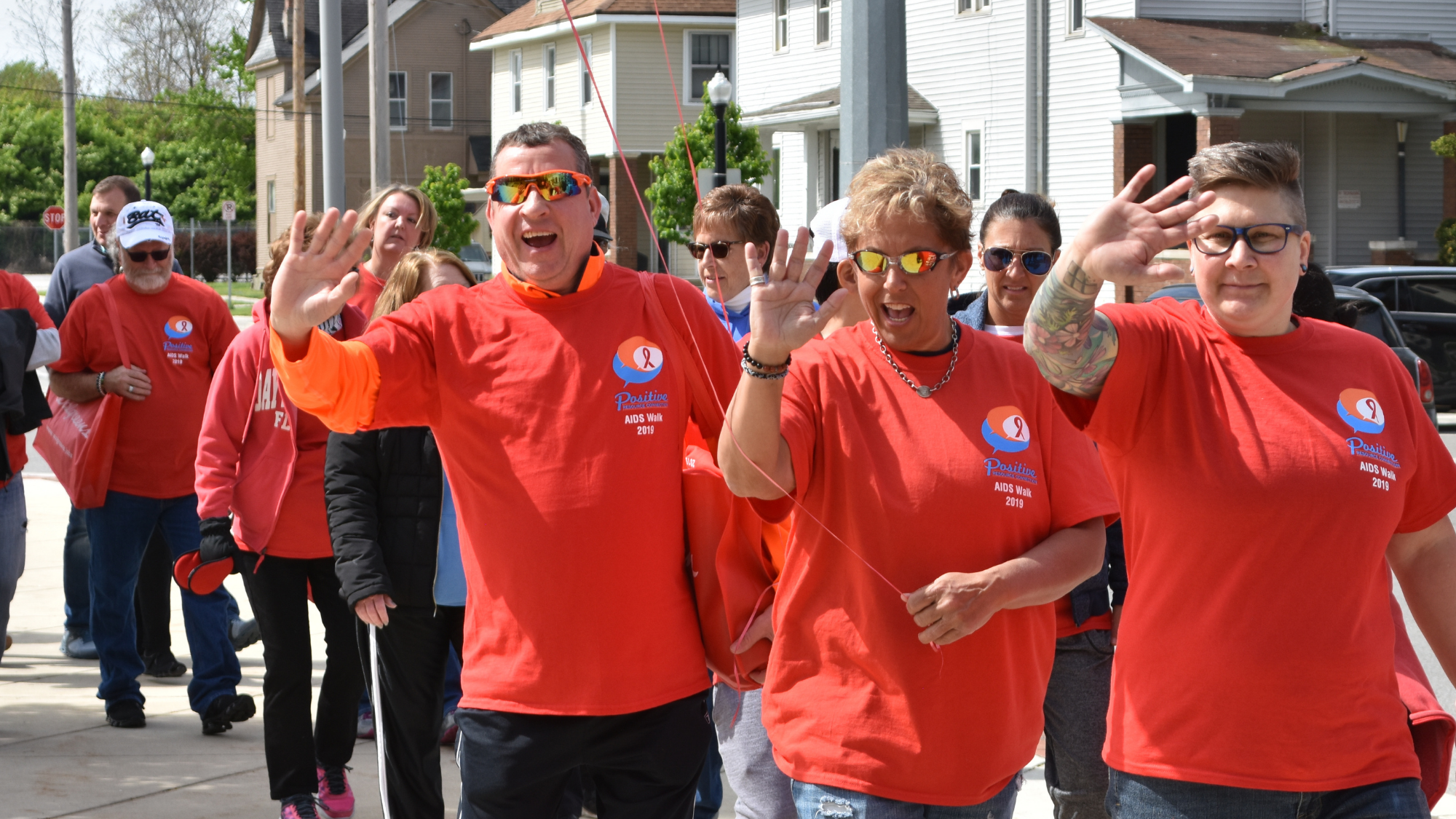People wearing red shirts smiling and waving at AIDS Walk
