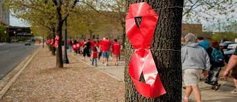 Red AIDS Ribbon tied around tree with AIDS Walk walkers in background