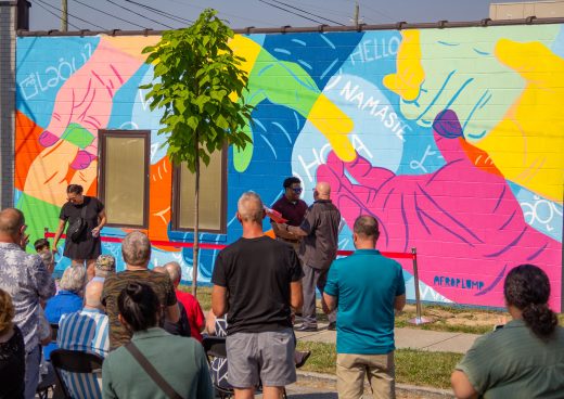 A crowd of people gather outside a building's mural