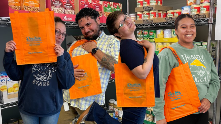 Four people holding orange PRC totes stand in front of stocked pantry shelves