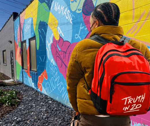 PRC team member with red backpack in front of agency mural